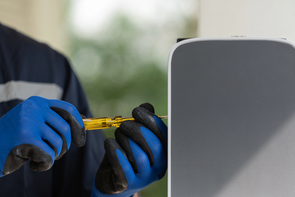 Person wearing blue gloves uses a screwdriver to install or repair an electric vehicle charging station.