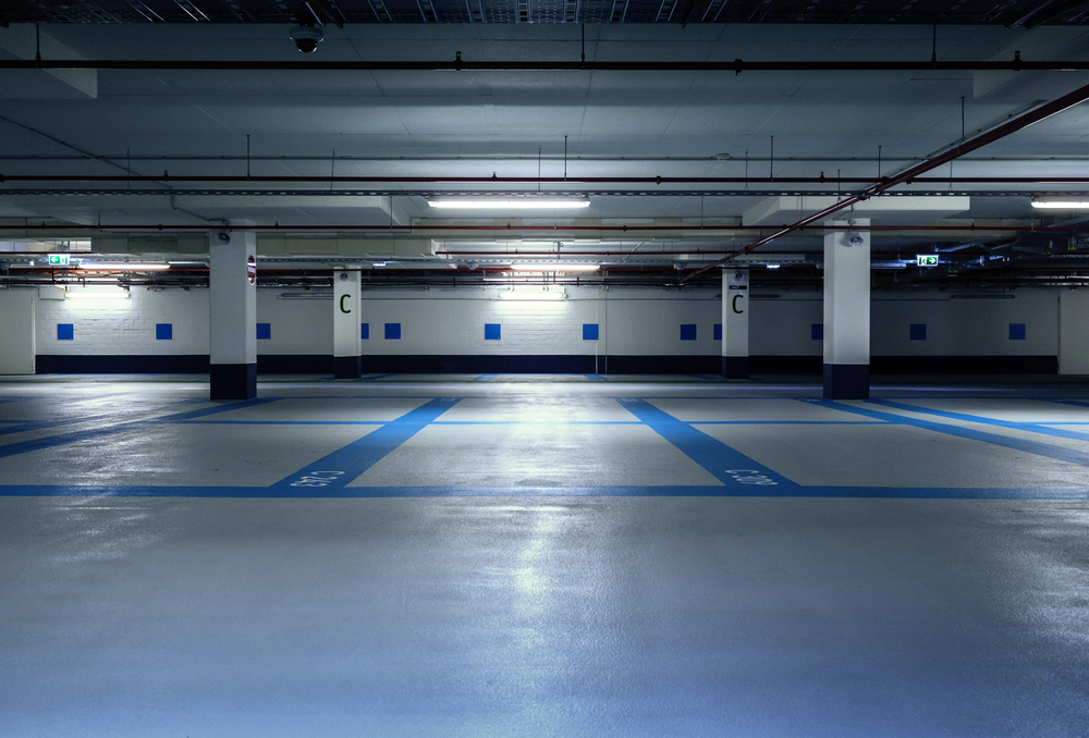Empty underground parking garage with blue and white markings, illuminated by overhead lights, and support columns labeled with the letter C